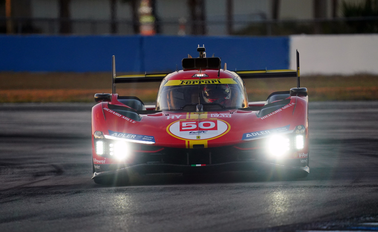 Front view of a red Ferrari racing car with number 50 and bright headlights on a racetrack.