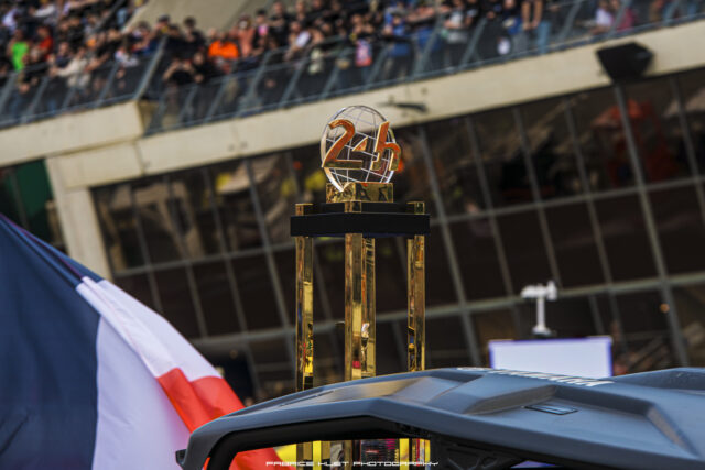 Tall golden trophy with a spherical metal globe and orange '246' numerals atop a black pedestal, set against a blurred race crowd.