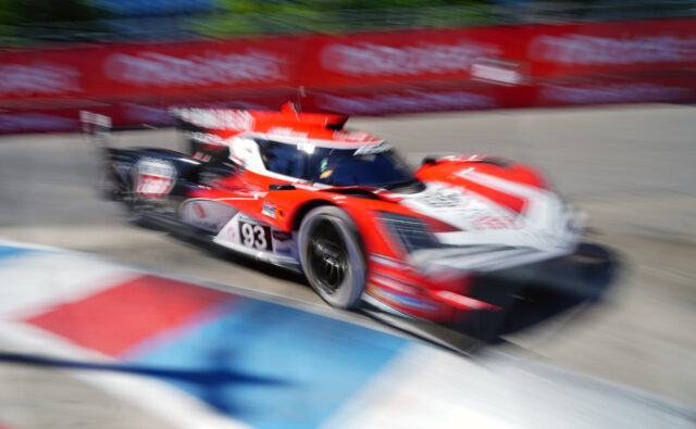 Red and white race car speeding around a track in motion blur, number 93 visible on the side barrier