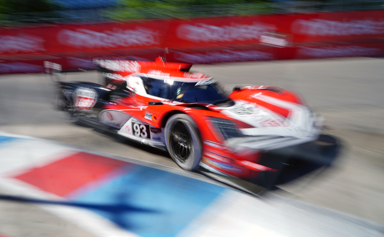 Red and white race car speeding around a track in motion blur, number 93 visible on the side barrier