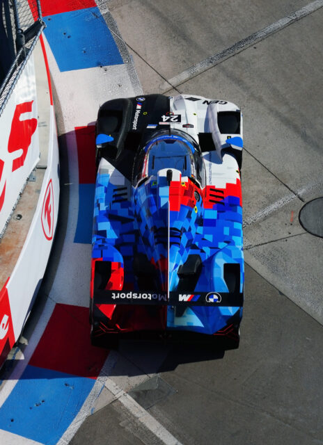 Top-down view of a prototype race car with blue, red, and white pixel-style livery on a race track for context and speed edge.