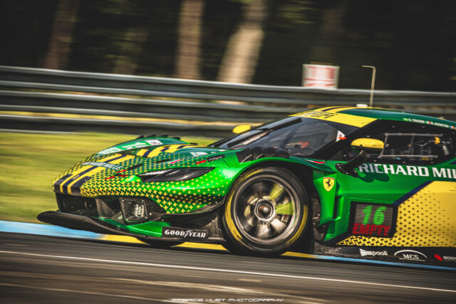 Green race car with yellow accents speeding along a race track, sponsor logos visible on the bodyplate
