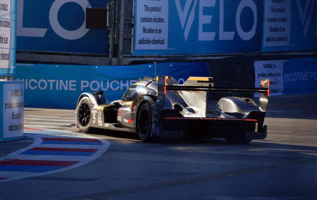 Prototype race car number 5 turning a corner on a street circuit, with blue sponsor banners in the background.