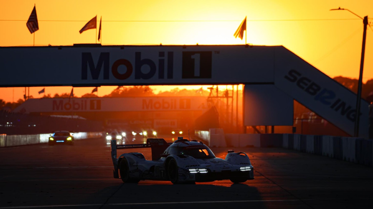 Race car on a track at sunset beneath Mobil 1 banners, headlights on