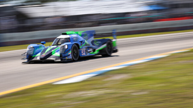 Blue-and-green endurance race car speeding along a track in motion blur, number 52 visible on the side edge of the car