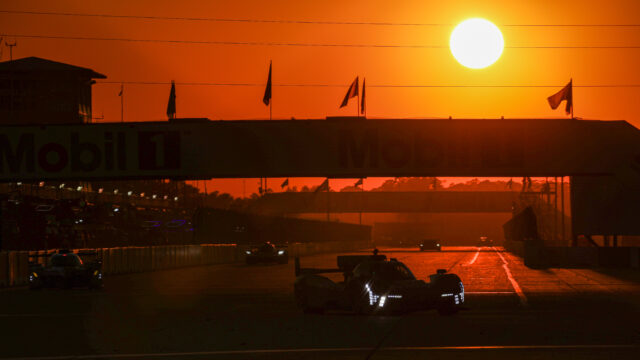 Sunset over a race track with silhouetted race cars and a Mobil 1 overpass against an orange sky.