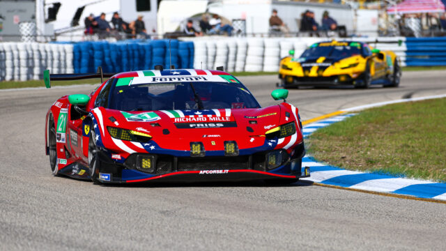 Red Ferrari race car with a red, white, and green livery leading a curved track, while a yellow race car pursues in the background behind blue and white barriers.