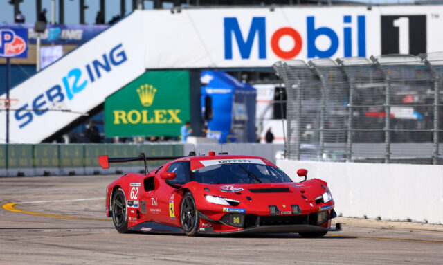 Red Ferrari race car #62 on a race track, with sponsor banners and a safety barrier nearby.