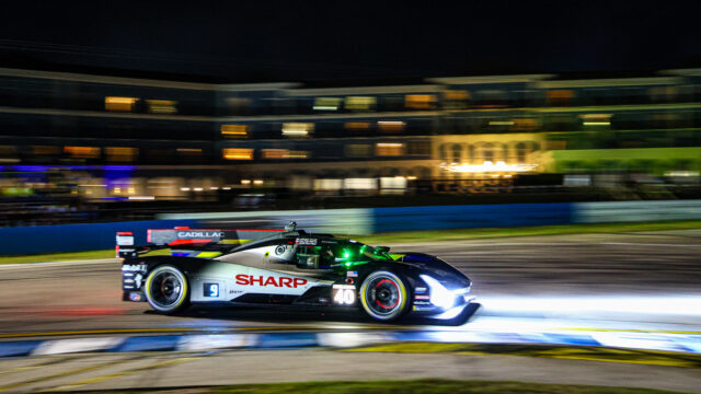Nighttime race car speeding on a well-lit track, car number 40 with Sharp and Cadillac livery in motion blur background.