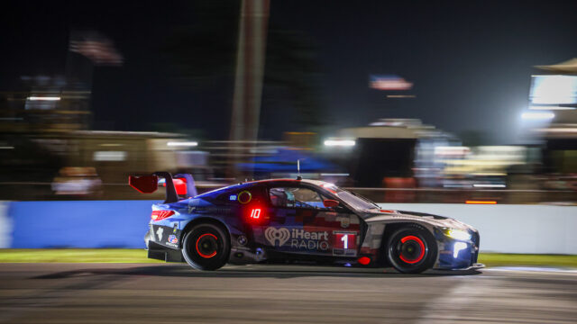 Nighttime race car in motion blur on a track, blue-red livery with iHeartRadio branding and the number 1 visible on the side.