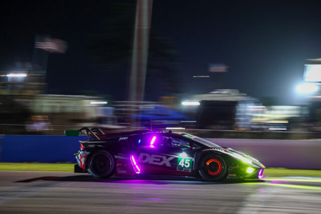 Nighttime race car with purple underglow speeding along track, number 45, with blurred background lights for motion.