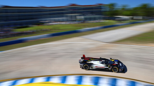 Race car number 40, Cadillac with Sharp branding, speeds along a sunlit race track in heavy motion blur.