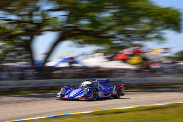 Blue and white Formula 1 race car speeding on a track with blurred green trees in the background