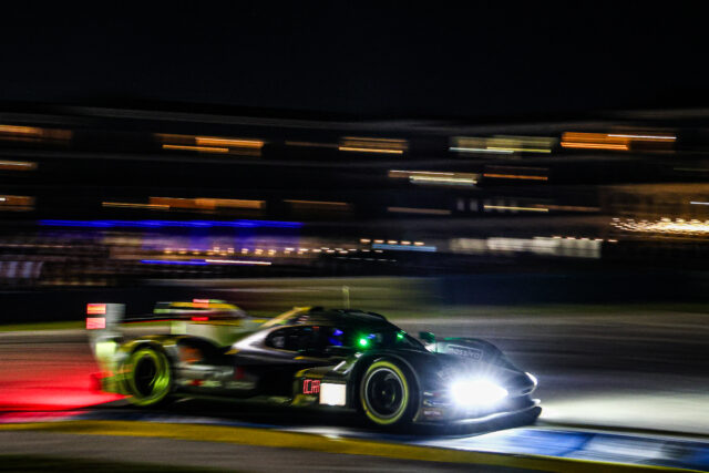 Nighttime race scene with blurred, speeding cars and bright headlights on a track at night as lights streak by.
