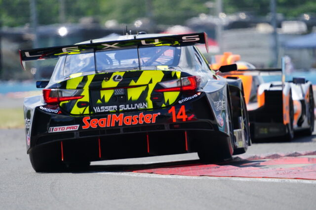 Rear view of a black race car with neon yellow camo livery and the number 14, sponsored by SealMaster, turning on a race track.