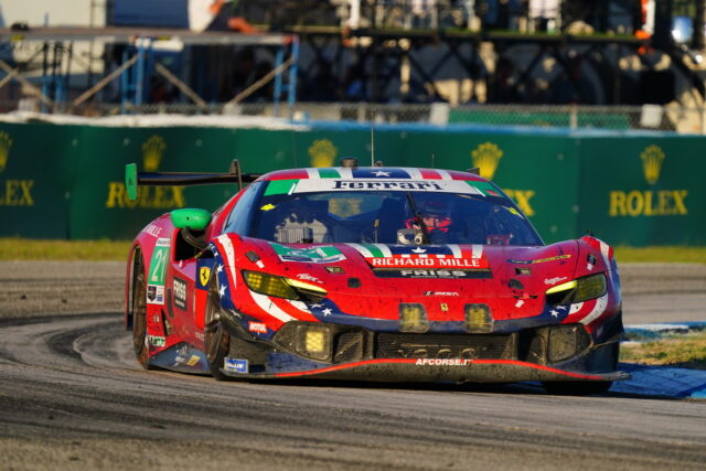 Red, white, and blue Ferrari race car number 21 on a curving track with sponsor banners in the background.