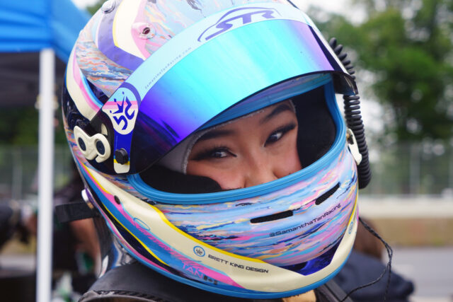 Close-up of a race driver wearing a colorful helmet with a blue visor, eyes smiling visible through the opening.